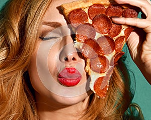 Woman hold big slice of pepperoni pizza slice blow kissing sign on blue mint background