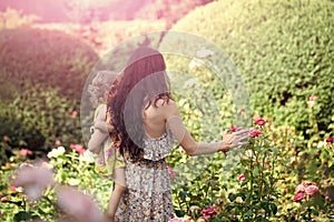 Woman hold child girl at blossoming roses on idyllic day