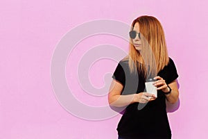 Woman hold a cup of coffee in hand. Girl with long hair drinking coffee on the city streets. Casual street fashion look