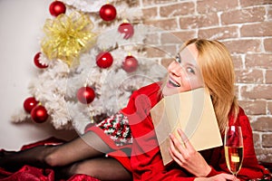 Woman hold glass champagne and book. Girl relax near christmas tree. Lady celebrate christmas alone. Winter holidays