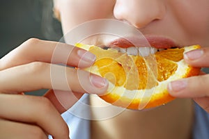 Woman hold in hand slice of chopped orange eats for breakfast with mouth in kitchen