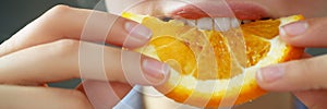 Woman hold in hand slice of chopped orange eats for breakfast with mouth in kitchen