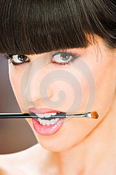 Woman hold make up brush between teeth