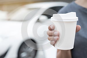 Woman hold paper cup coffee of hot in hand while standing car on the side before driving a vehicle in the morning sunlight