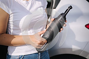 Woman hold portable vacuum cleaner in front of car. Attractive young woman prepare for cleaning in garage. Close-up of