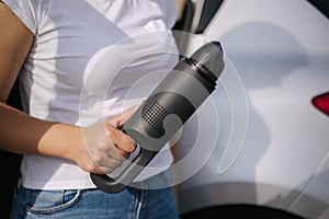 Woman hold portable vacuum cleaner in front of car. Attractive young woman prepare for cleaning in garage. Close-up of