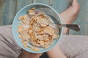 Woman hold sky blue colored bowl of tasty cereal corn flakes