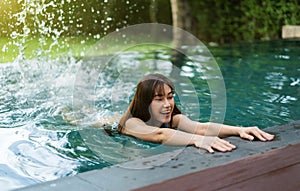 Woman hold on to the edge of the swimming pool and splashing water with her feet
