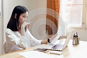 Woman holding agreement documents and using laptop on table in office room, to plan advance budget.