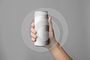 Woman holding aluminum can with beverage on grey background, closeup.