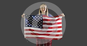 Woman holding a american flag with pole, stars and stripes on gray background.