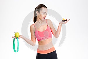 Woman holding apple, mesuring tape and cake making a choice