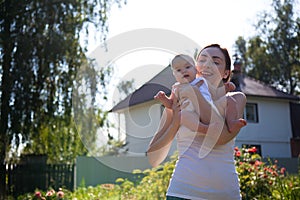 Woman holding baby on arms against a house