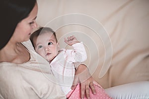 Woman holding baby wear pajamas lying on mother hand wake up in bed.