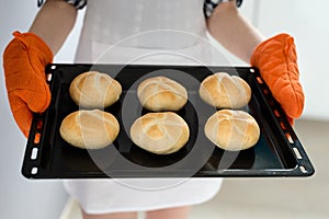 Woman holding baking tray with baked bread rolls.