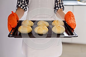 Woman holding a baking tray with freshly baked bread rolls.