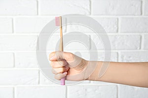 Woman holding bamboo toothbrush against brick wall, closeup