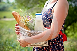 Woman holding a basket with bread, milk and flowers in a summer