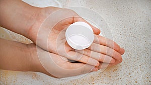 Woman holding bath bomb over water with foam, closeup