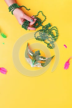 Woman holding beads on bright yellow background, top view, copy space. Border with traditional Mardi gras beads, masks, feathers
