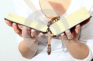 Woman holding a bible and rosary beads cross in her hands