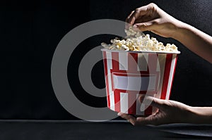 Woman holding a big bucket of salty hot popcorn against dark background.Empty space for text