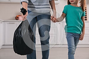 Woman holding bin bag full of garbage in kitchen, closeup