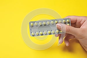 Woman holding birth control pills on yellow background, closeup