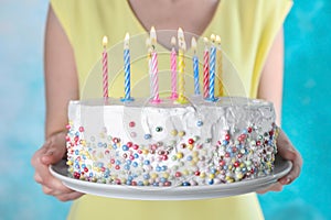 Woman holding birthday cake with burning candles on light blue background,
