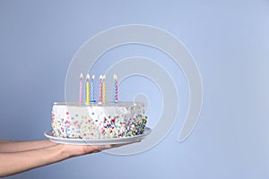 Woman holding birthday cake with burning candles on light blue background, closeup.