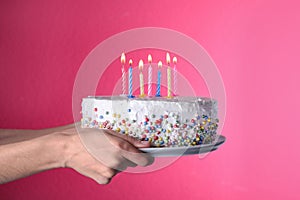 Woman holding birthday cake with burning candles on pink background