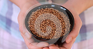 A woman holding a black bowl with buckwheat inside it in her hands.