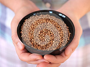 A woman holding a black bowl with buckwheat inside it in her hands