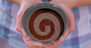 A woman holding a black bowl with organic cocoa powder in it in her hands.