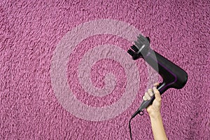 Woman holding black hair dryer against decorative hairy background.Empty space