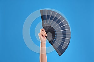 Woman holding black hand fan on light blue  background, closeup