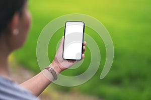 A woman holding black mobile phone with blank desktop screen with blur green nature background