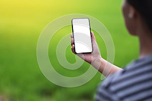 A woman holding black mobile phone with blank desktop screen with blur green nature background