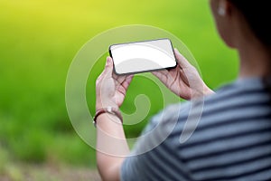 A woman holding black mobile phone with blank desktop screen with blur green nature background