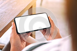 A woman holding black mobile phone with blank white screen horizontally in cafe