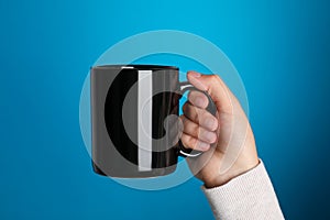 Woman holding black mug on light blue background, closeup