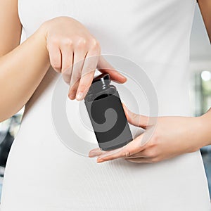 Woman holding black plastic jar in hands for cosmetics over white t shirt