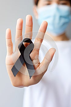 Woman holding black Ribbon for Melanoma and skin cancer, Vaccine injury awareness month, grief and rest in peace. Healthcare and