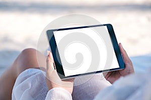 A woman holding a black tablet pc with blank desktop screen while laying down on beach chair on the beach