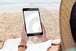 A woman holding a black tablet pc with blank desktop screen while lying down on a beach chair