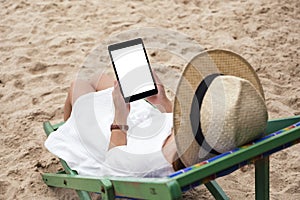 A woman holding a black tablet pc with blank desktop screen while lying down on a beach chair