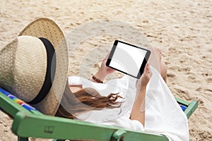 A woman holding a black tablet pc with blank desktop screen while lying down on a beach chair