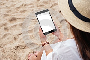 A woman holding a black tablet pc with blank desktop screen while sitting on a beach chair