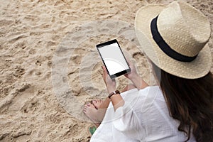 A woman holding a black tablet pc with blank desktop screen while sitting on a beach chair