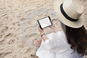 A woman holding a black tablet pc with blank desktop screen while sitting on a beach chair